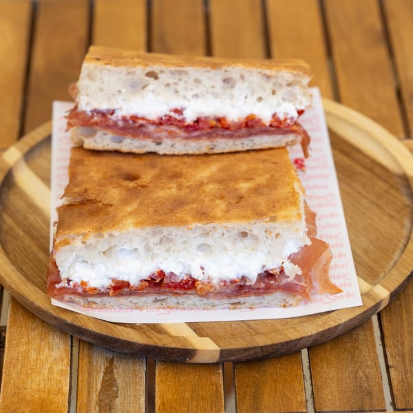 Two halves of a focaccia sandwich with prosciutto, ricotta, and roasted red peppers on a wooden plate.