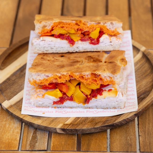 Two focaccia sandwiches with turkey, cheese, and colorful roasted peppers on a wooden tray.