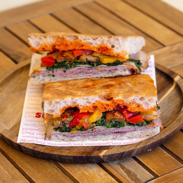 Two halves of a focaccia sandwich filled with meat, cheese, spinach, and roasted peppers on a wooden tray.