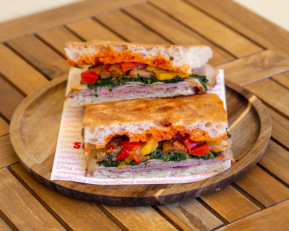 Two halves of a focaccia sandwich filled with meat, cheese, spinach, and roasted peppers on a wooden tray.