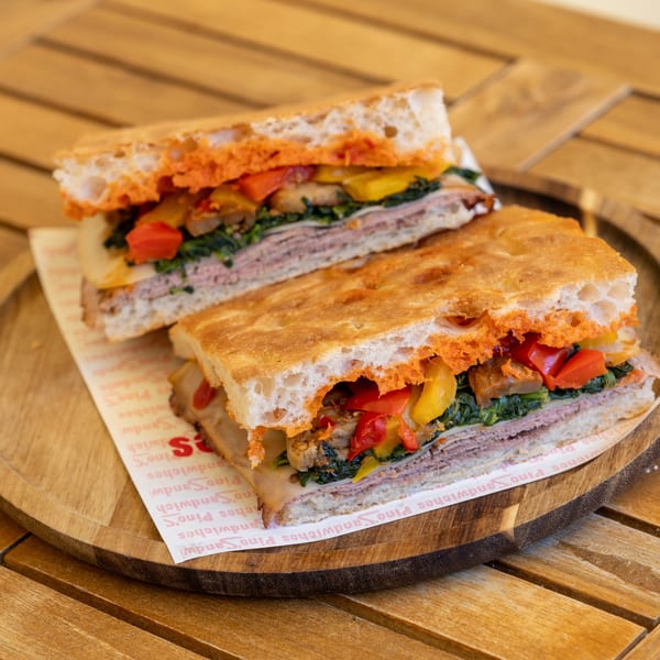 Two halves of a focaccia sandwich with meat, cheese, spinach, and roasted peppers on a wooden tray.