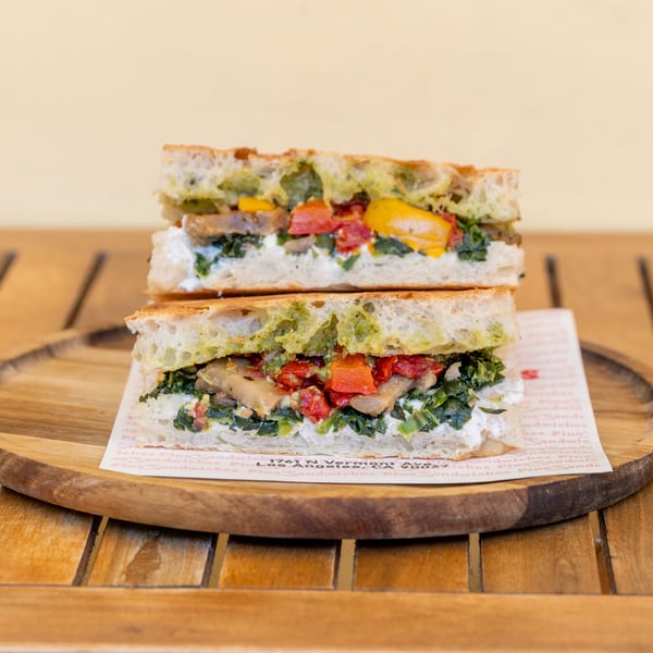 Two halves of a focaccia sandwich with pesto, spinach, roasted peppers, and mushrooms on a wooden plate.