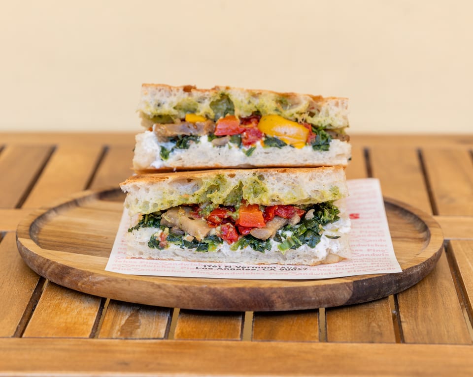 Two halves of a focaccia sandwich with pesto, spinach, roasted peppers, and mushrooms on a wooden plate.