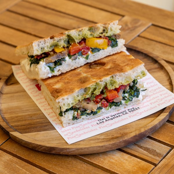 A focaccia sandwich, cut in half, filled with vegetables and cheese, on a wooden plate.