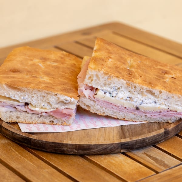 Two halves of a focaccia sandwich with ham, cheese, and ricotta on a wooden board.