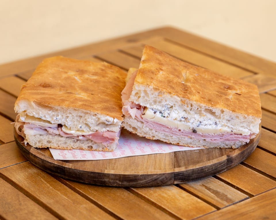 Two halves of a focaccia sandwich with ham, cheese, and ricotta on a wooden board.