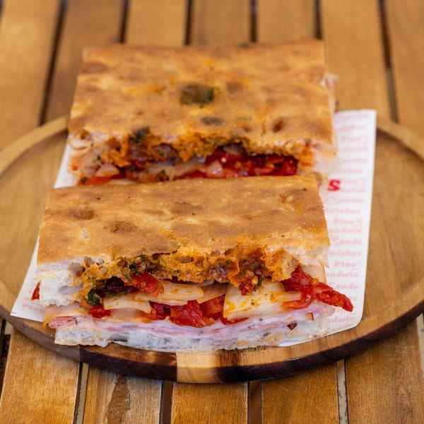 Two halves of a focaccia sandwich filled with ham, cheese, sun-dried tomatoes, and onions.