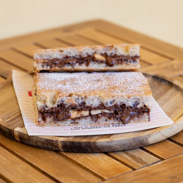 Two halves of a Nutella and banana sandwich, dusted with powdered sugar, on a wooden plate.